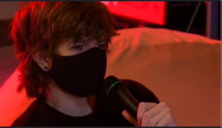 A photo of Ranboo from their Valentine's Day Livestream (I have it linked.) He is holding a microphone to their face. He has long hair in this photo with bangs that sweep over their forehead. He is wearing a black mask.